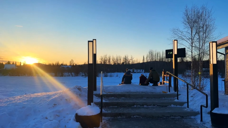 People Sitting on Steps, Watching the Sunset Over a Snowy Alaska Landscape