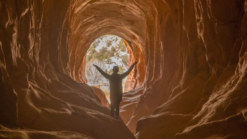 Person silhouetted with arms raised inside Belly of the Dragon cave tunnel in southern Utah