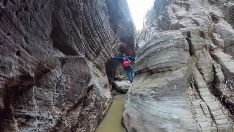 Adventurer balancing on rock ledge in Hidden Canyon, surrounded by tall narrow cliffs