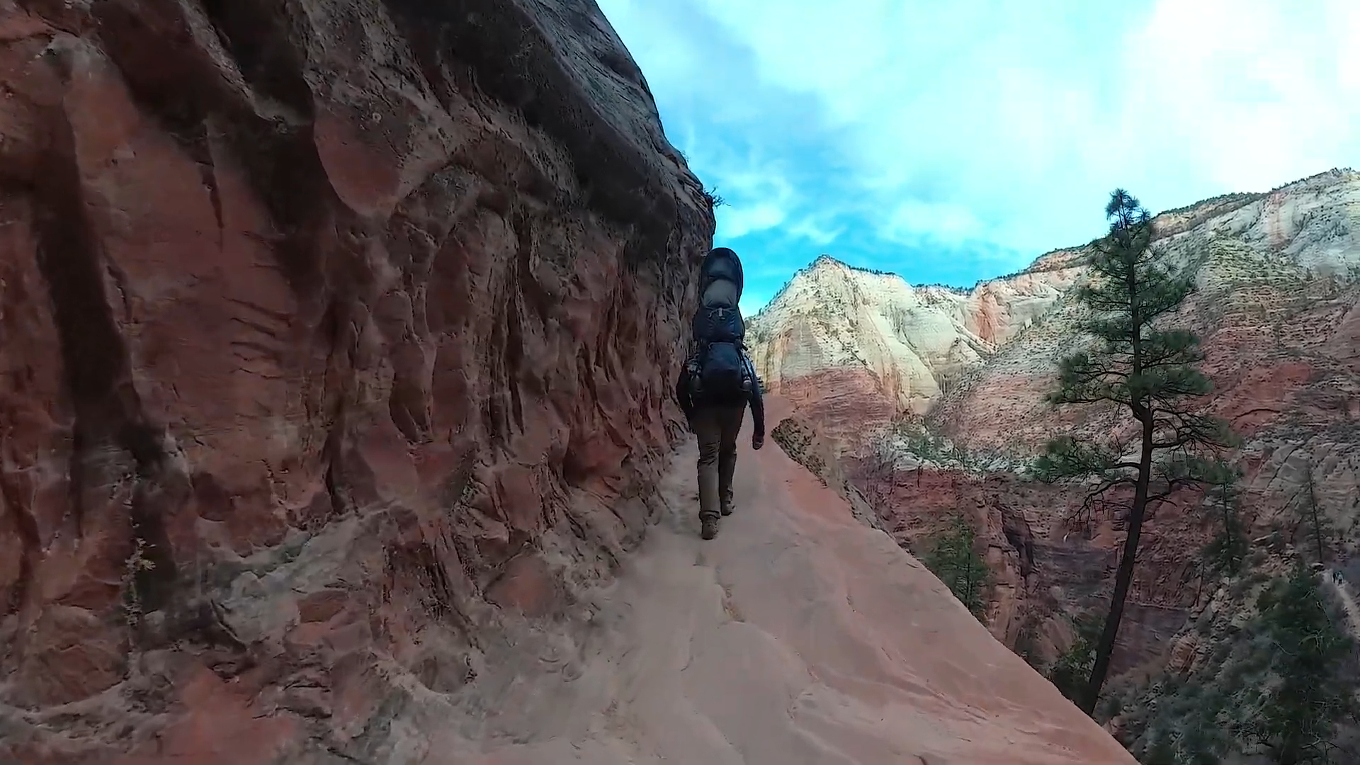 A hiker walking along a narrow sandstone trail in Hidden Canyon, Zion National Park, with steep cliffs and scenic views