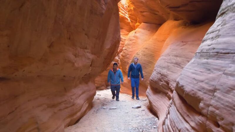 Two hikers walking through the winding red sandstone walls of Peekaboo Canyon in southern Utah