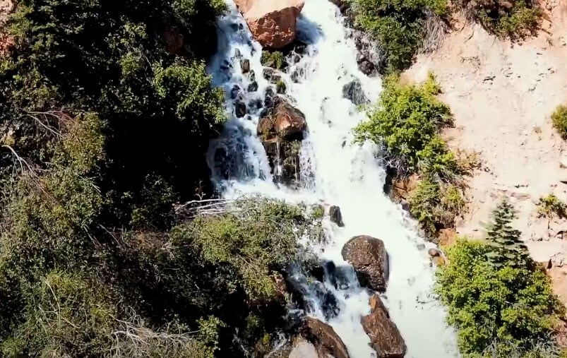 Cascading water tumbles over rocky terrain, surrounded by lush greenery