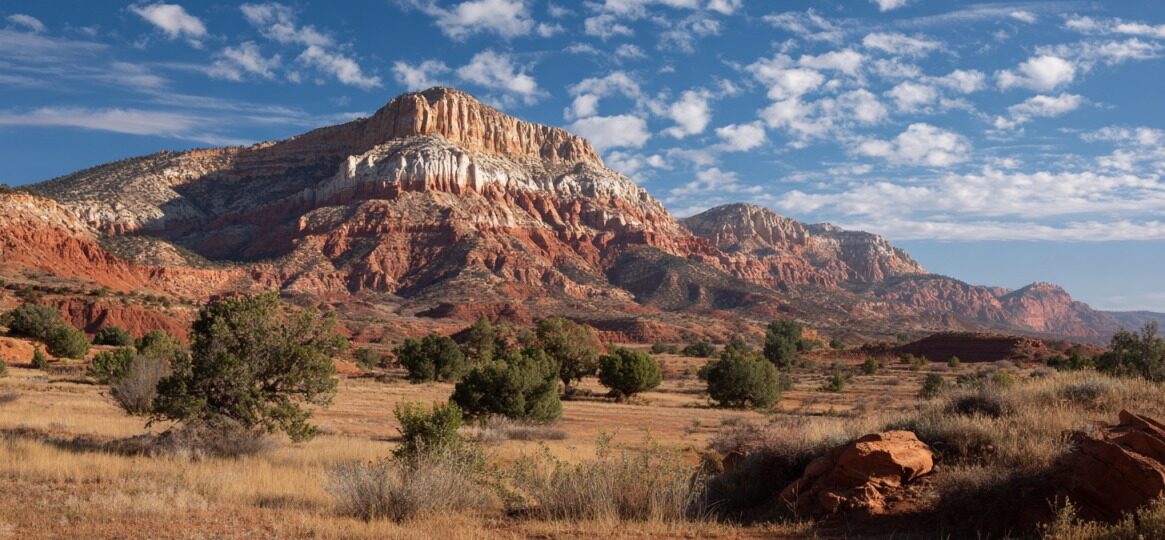Panoramic view of colorful red rock cliffs and desert terrain under a partly cloudy blue sky near Kanab