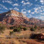 Panoramic view of colorful red rock cliffs and desert terrain under a partly cloudy blue sky near Kanab