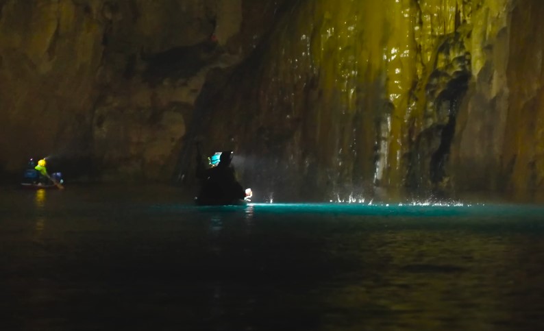Explorers navigate a subterranean river, illuminated by headlamp beams