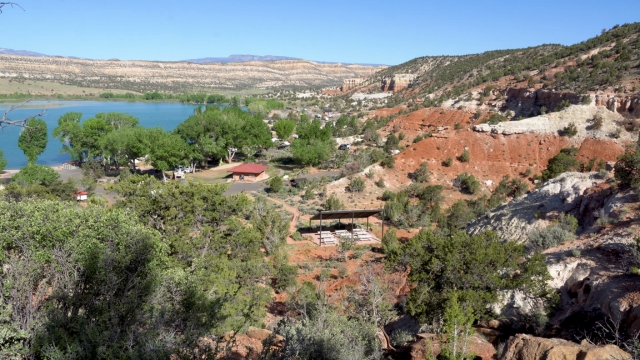 Escalante Petrified Forest with red hills, green trees, and a blue lake under clear skies