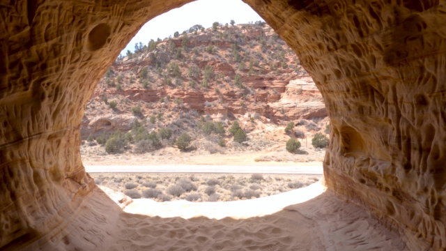 View from inside Moqui Caverns showing sandy floor and red rock landscape outside
