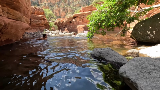 A swimmer enjoys the cool water surrounded by red rocks and trees at Sedona’s swimming holes