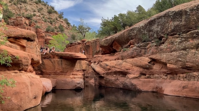People sitting on red rock ledges above the water at The Crack on Wet Beaver Creek via Bell Trail