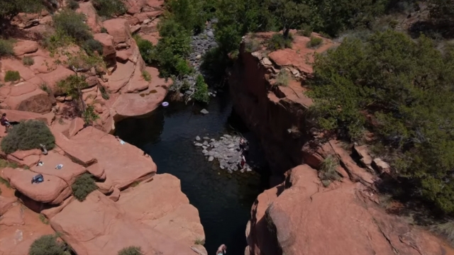 A natural swimming hole surrounded by red rock cliffs and greenery in Sedona