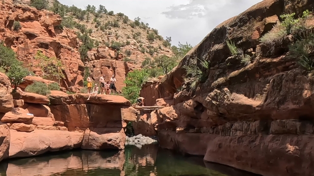 People standing on red rock ledges above the water at Sedona’s swimming holes