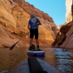 A man paddles through a narrow canyon on a paddle board