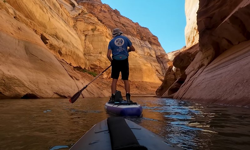 A man paddles through a narrow canyon on a paddle board