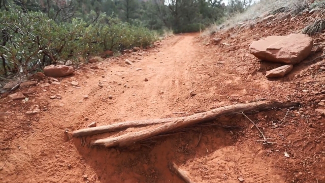 A red dirt trail in Sedona with small logs across the path and red rock lining the side