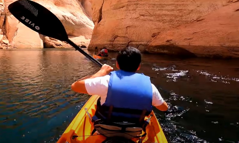 A man paddles a kayak through a narrow canyon surrounded by steep rock walls 