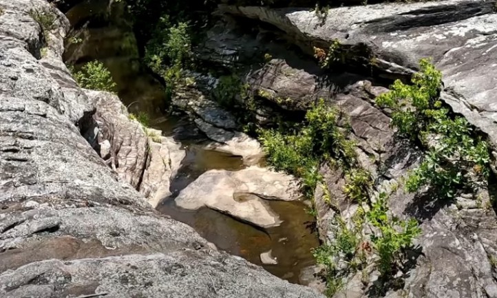 Water-worn rock formations cradle a small, still pool amidst jagged grey stone cliffs