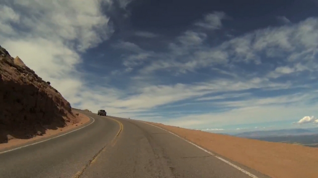 A car ascends the winding Pikes Peak Highway