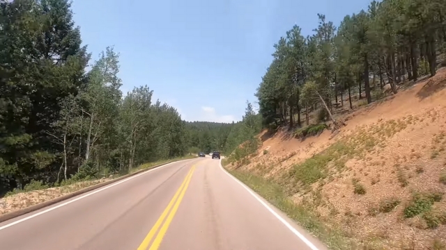 Cars drive along a forested section of the Pikes Peak Highway on a clear summer day