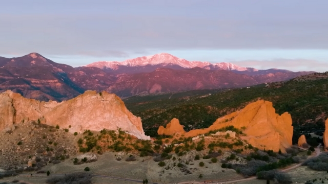 Pikes Peak at sunrise with its summit glowing above Garden of the Gods red rock formations in Colorado Springs