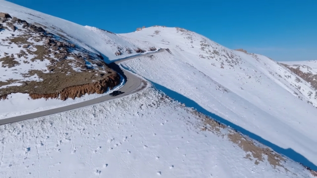 A car drives along the snow-covered road near the summit of Pikes Peak under a clear blue sky