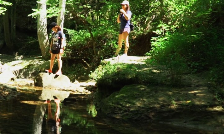 Two women standing in front of a pond in a green forest