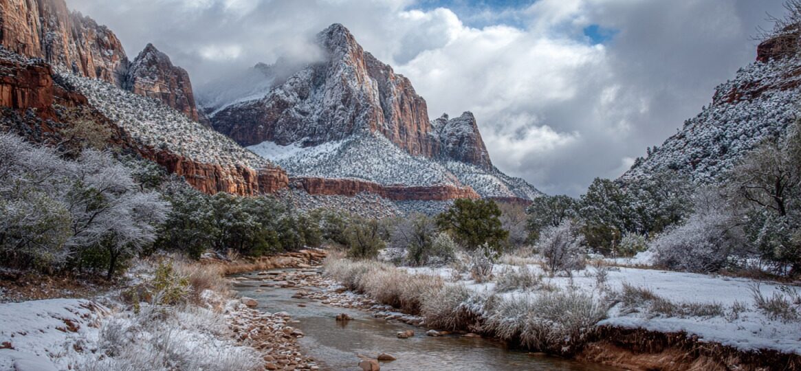 River flowing through a snowy canyon with towering red rock cliffs and clouds overhead