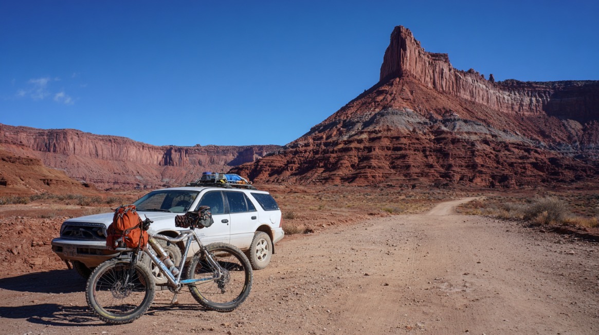 Loaded vehicle and bike parked on a dirt road in Canyonlands desert terrain