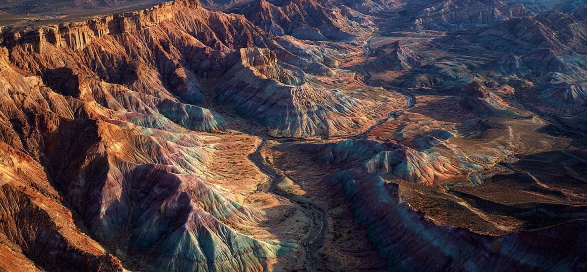 Aerial view of layered desert hills with swirling bands of red, blue, green, and tan bentonite clay