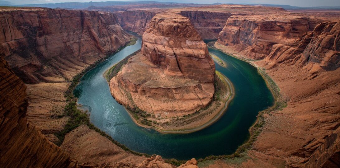 High vantage view of a dramatic horseshoe shaped canyon with a green river curving around a massive sandstone rock formation