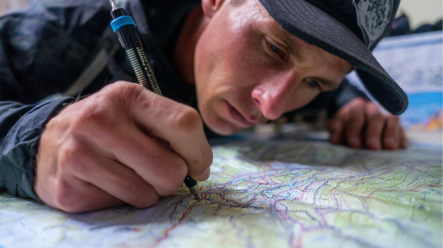 Close up of a hiker studying and marking a detailed topographic map with a pencil