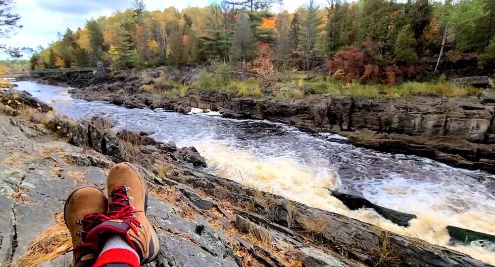 Hiking boots resting on rock above a rushing river gorge with autumn trees
