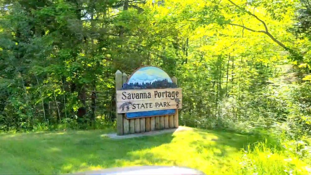 Wooden entrance sign for Savanna Portage State Park surrounded by green forest