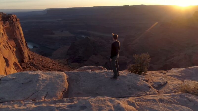 Person stands on a cliff at Dead Horse Point State Park, Utah, looking over a canyon at sunset