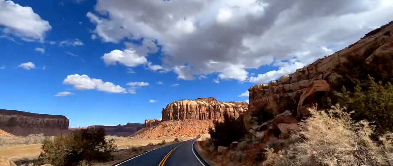 Scenic road winding through red rock desert landscapes in Southern Utah under a blue sky with clouds