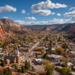 Small town nestled between red rock formations with trees and buildings under a blue sky