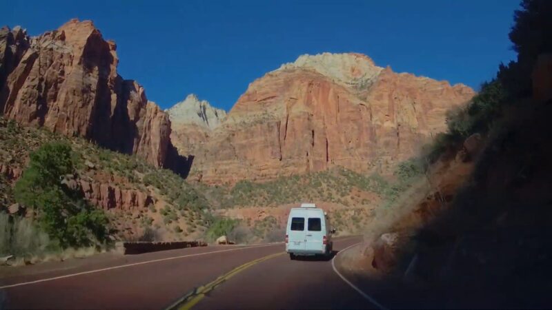 Van driving along Zion-Mount Carmel Highway with steep red rock cliffs on both sides