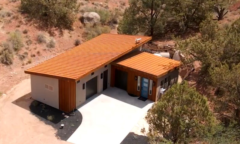 A modern, flat-roofed house with wooden accents sits in a desert landscape
