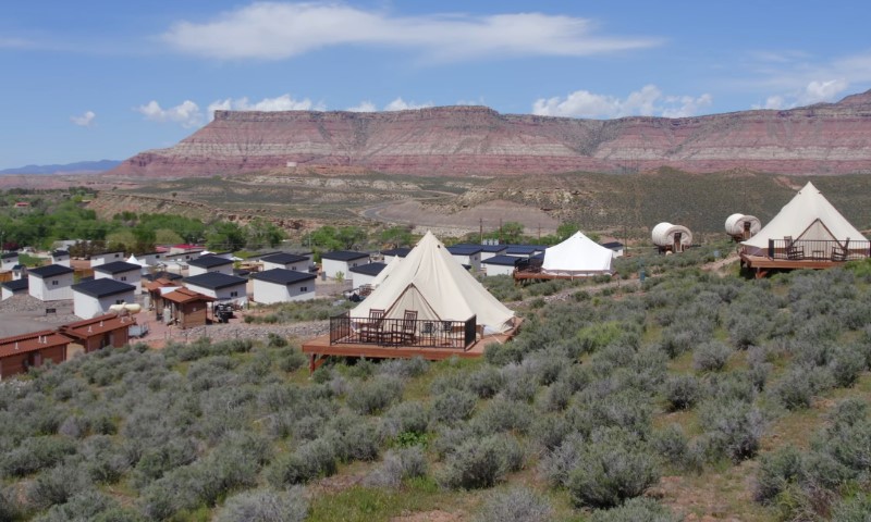 Tents and covered wagons are set on wooden decks amid sagebrush under a wide sky