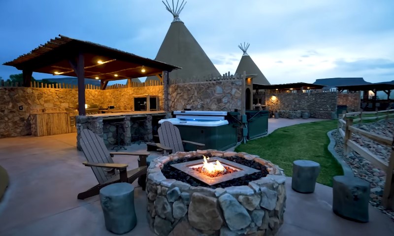 Outdoor patio with a stone fire pit, Adirondack chairs, and a hot tub under a wooden pergola